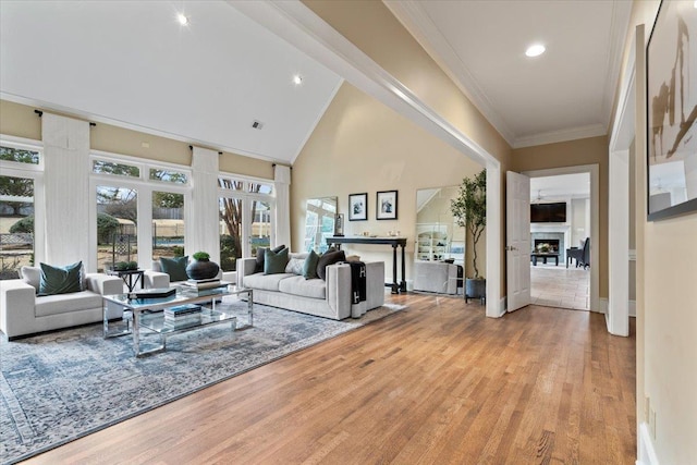 living area with ornamental molding, light wood-type flooring, a fireplace, high vaulted ceiling, and recessed lighting