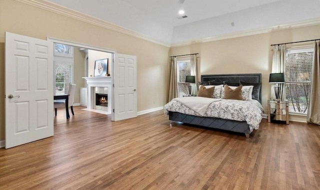 bedroom with baseboards, visible vents, a fireplace with flush hearth, ornamental molding, and wood finished floors