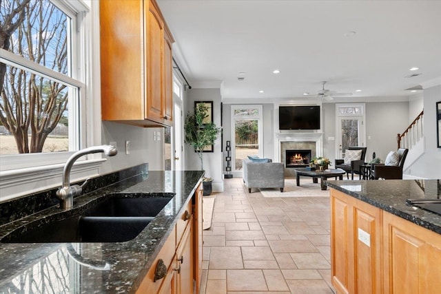 kitchen with a lit fireplace, crown molding, light brown cabinets, a sink, and recessed lighting