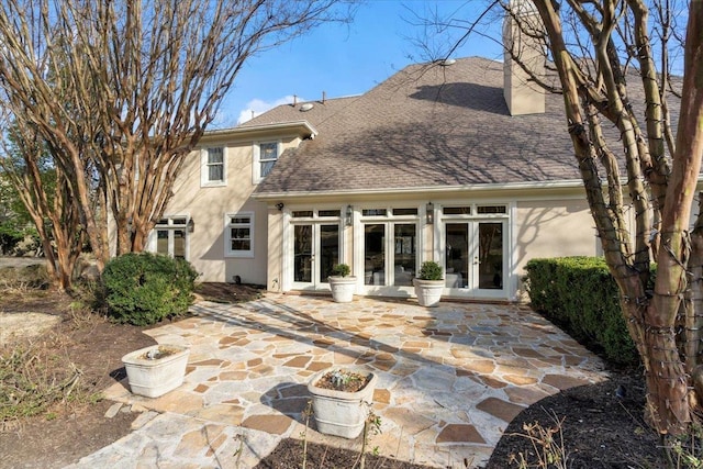 rear view of house with stucco siding, roof with shingles, a patio, and french doors