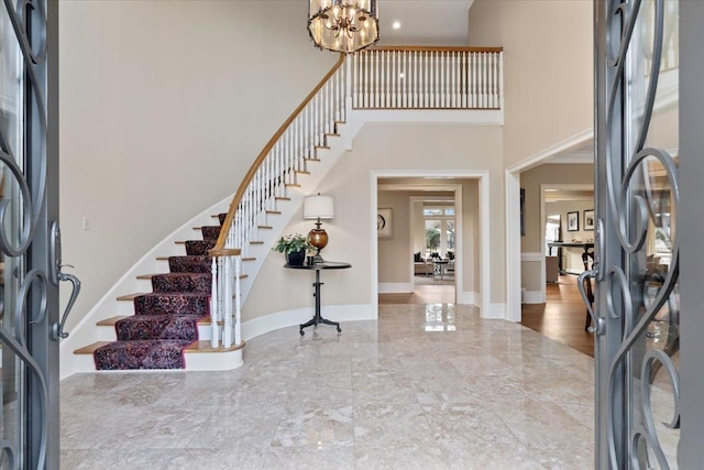 foyer featuring a chandelier, a towering ceiling, baseboards, stairs, and marble finish floor