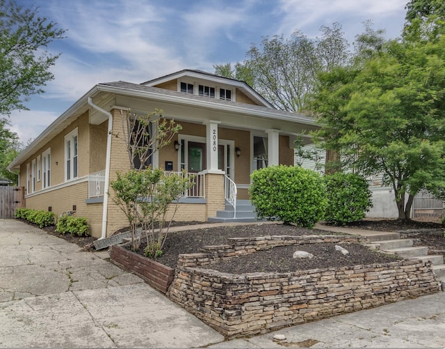 view of front of home featuring brick siding, a porch, and fence