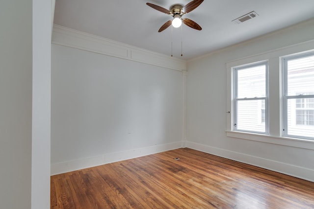 unfurnished room with visible vents, crown molding, baseboards, and wood finished floors