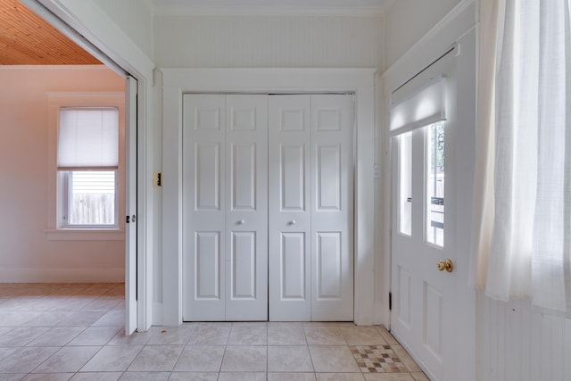 entryway with light tile patterned floors and crown molding