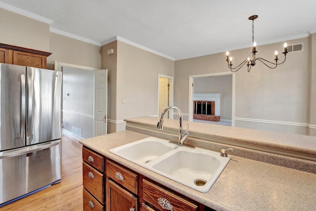 kitchen featuring light wood finished floors, visible vents, brown cabinets, freestanding refrigerator, and a sink