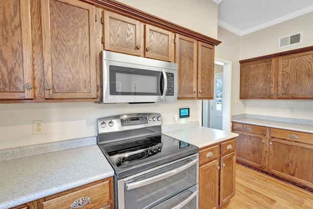 kitchen with visible vents, appliances with stainless steel finishes, ornamental molding, light countertops, and light wood-type flooring