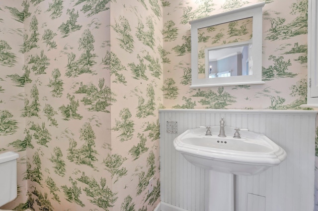 bathroom with wainscoting, a sink, toilet, and wallpapered walls