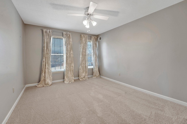 empty room with a textured ceiling, carpet flooring, visible vents, a ceiling fan, and baseboards