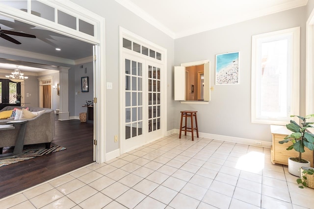 spare room featuring crown molding, decorative columns, light tile patterned floors, baseboards, and ceiling fan with notable chandelier