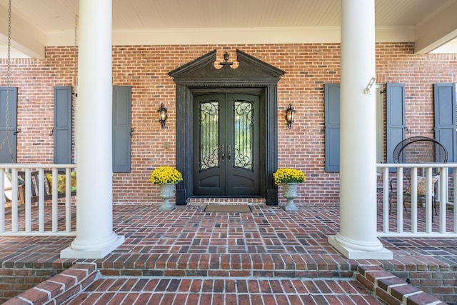 view of exterior entry featuring french doors, a porch, and brick siding