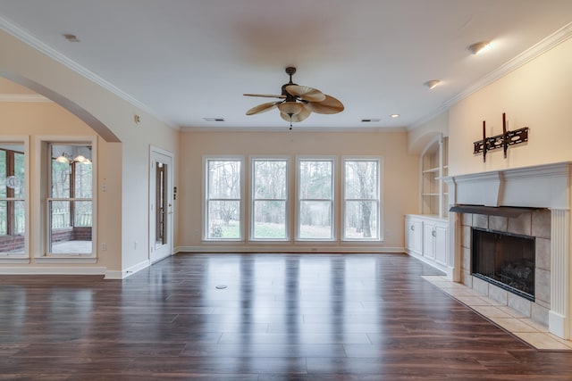 unfurnished living room featuring ceiling fan, wood finished floors, baseboards, ornamental molding, and a tiled fireplace