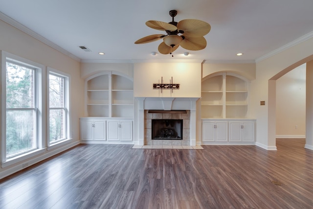 unfurnished living room featuring visible vents, built in features, a tiled fireplace, ornamental molding, and wood finished floors