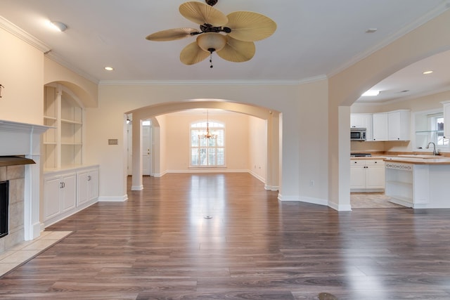 unfurnished living room featuring arched walkways, a fireplace, wood finished floors, built in features, and crown molding