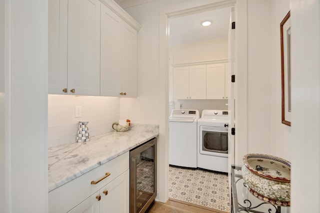 clothes washing area featuring light wood-type flooring, wine cooler, independent washer and dryer, and cabinet space