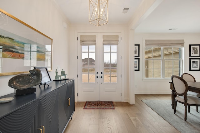 foyer featuring french doors, light wood finished floors, an inviting chandelier, ornamental molding, and baseboards