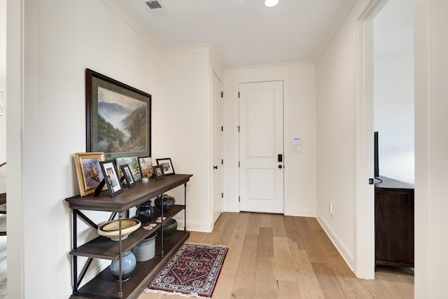 foyer with light wood-style flooring, visible vents, baseboards, and ornamental molding