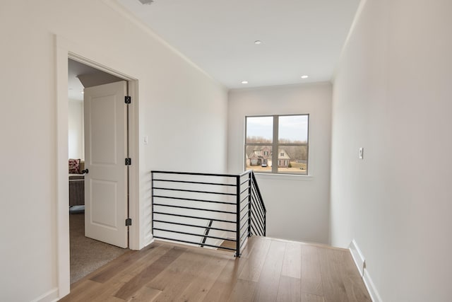 hallway featuring baseboards, wood finished floors, an upstairs landing, and recessed lighting