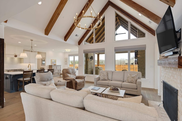 living room with light wood-style floors, a fireplace, high vaulted ceiling, and an inviting chandelier