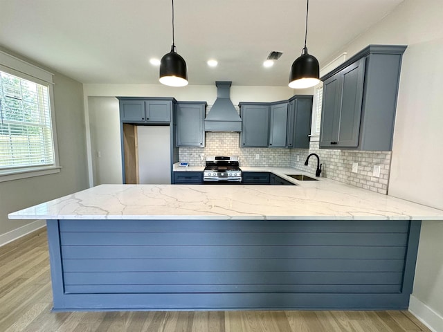 kitchen featuring light stone counters, a peninsula, a sink, stainless steel gas range, and custom exhaust hood