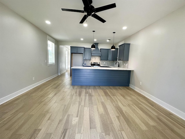 kitchen with light wood finished floors, tasteful backsplash, light countertops, premium range hood, and a peninsula