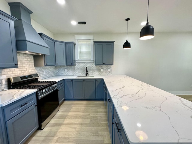 kitchen with blue cabinetry, custom exhaust hood, a sink, light stone countertops, and stainless steel gas range