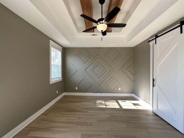 empty room with a tray ceiling, a barn door, wood finished floors, and baseboards