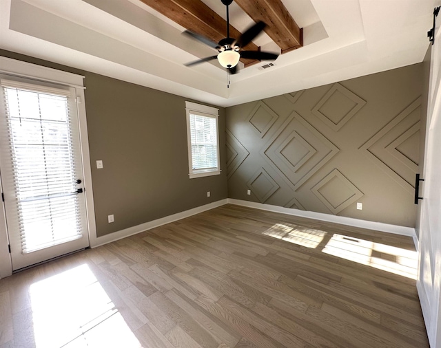 empty room featuring baseboards, a ceiling fan, light wood-style flooring, beamed ceiling, and a tray ceiling