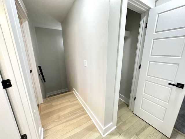 hall featuring light wood-style flooring, baseboards, and an upstairs landing