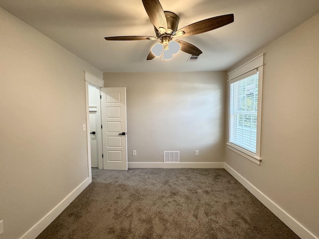 spare room featuring dark colored carpet, visible vents, and baseboards