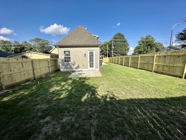 back of house with a fenced backyard, a lawn, a patio, and roof with shingles