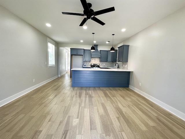 kitchen with decorative backsplash, a peninsula, light countertops, light wood-type flooring, and premium range hood