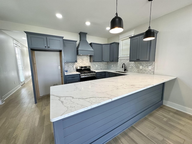 kitchen with stainless steel range with gas cooktop, custom exhaust hood, tasteful backsplash, light stone countertops, and a peninsula