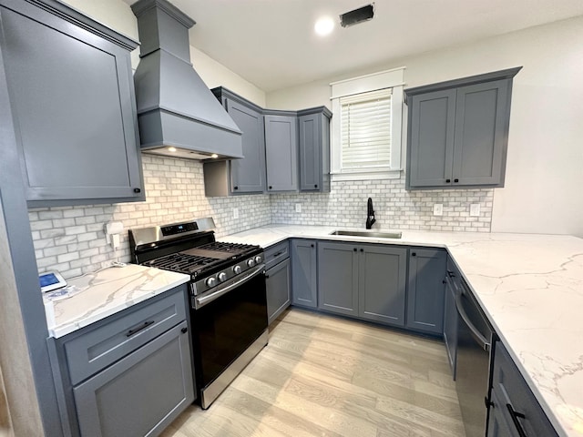 kitchen featuring custom range hood, light stone counters, stainless steel appliances, light wood-type flooring, and a sink