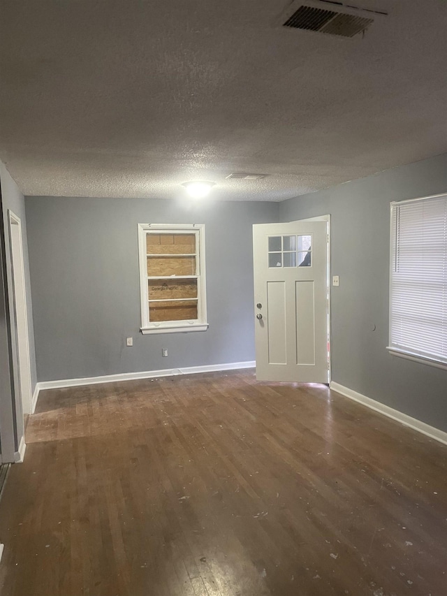 foyer entrance featuring a textured ceiling, wood finished floors, visible vents, and baseboards