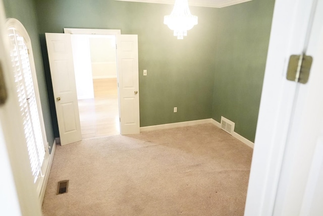 carpeted spare room featuring baseboards, an inviting chandelier, visible vents, and a healthy amount of sunlight