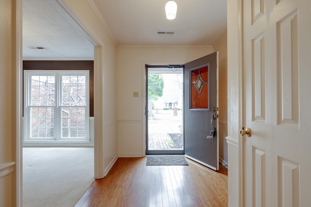 doorway with baseboards, ornamental molding, visible vents, and light wood-style floors