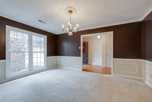 carpeted empty room featuring a textured ceiling, a notable chandelier, visible vents, ornamental molding, and wainscoting