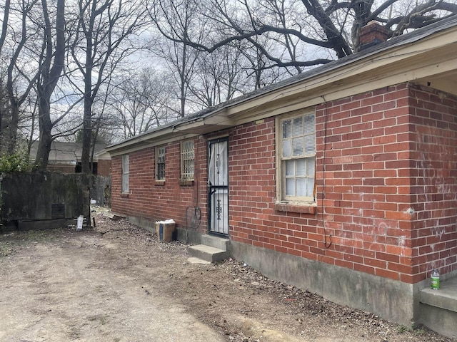 view of side of property with entry steps, dirt driveway, a chimney, and brick siding