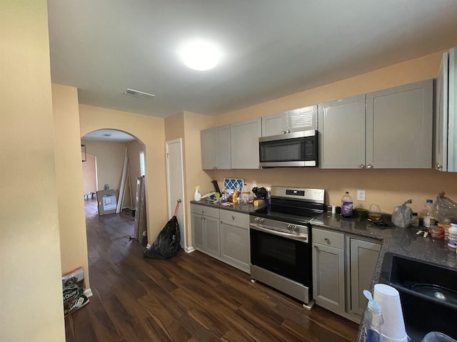 kitchen featuring arched walkways, stainless steel appliances, gray cabinets, visible vents, and dark wood-type flooring