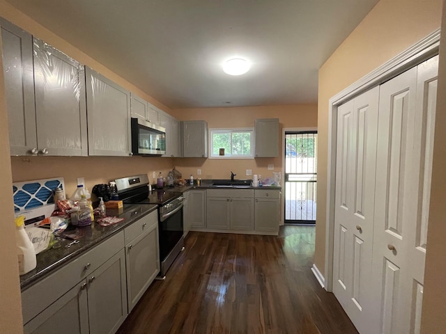 kitchen featuring stainless steel appliances, dark countertops, dark wood finished floors, and a sink