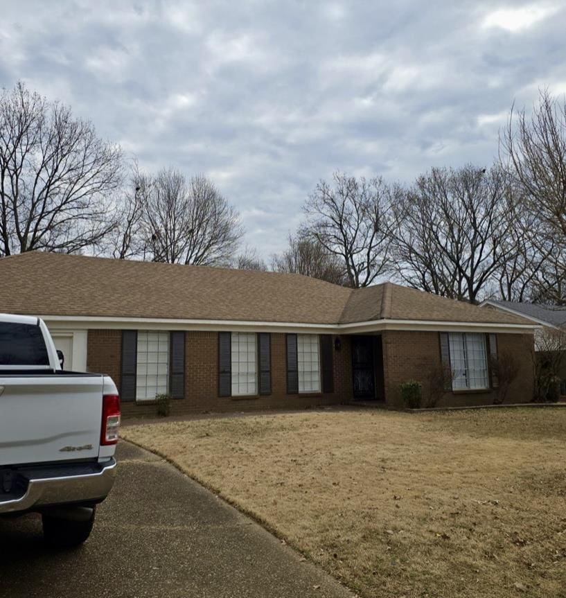 ranch-style house featuring a shingled roof, brick siding, and a front lawn