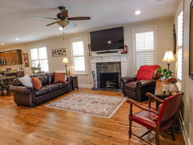 living area with a ceiling fan, a tiled fireplace, ornamental molding, and wood finished floors