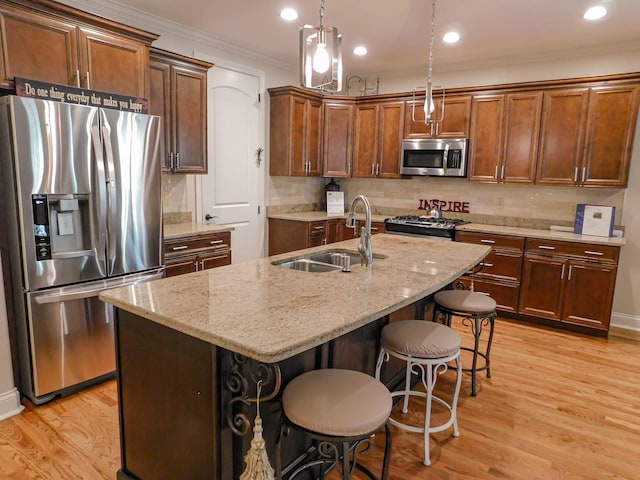 kitchen featuring light wood finished floors, stainless steel appliances, ornamental molding, and a sink