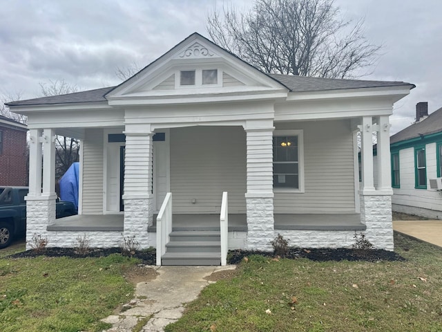 view of front of house featuring covered porch, a shingled roof, and a front lawn