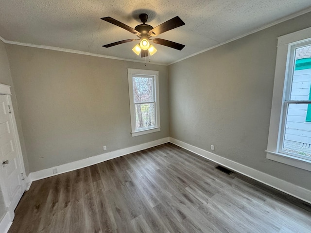 spare room featuring crown molding, visible vents, a textured ceiling, wood finished floors, and baseboards