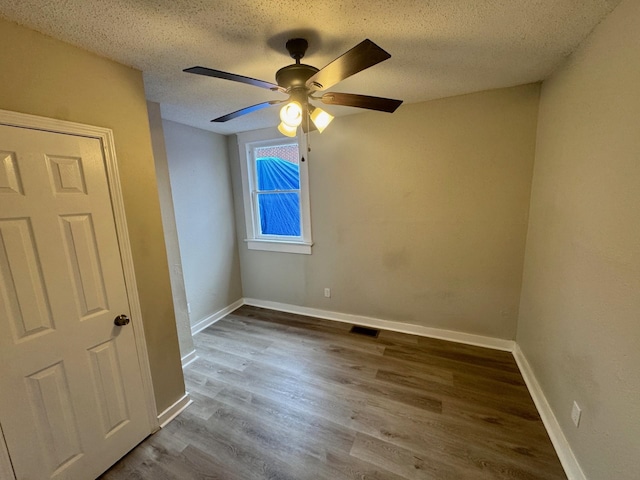 unfurnished room featuring visible vents, a ceiling fan, a textured ceiling, wood finished floors, and baseboards