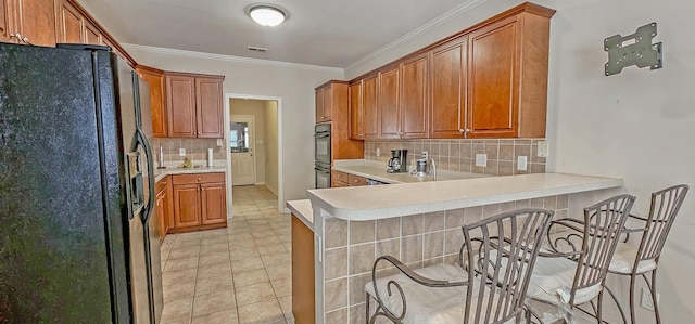 kitchen featuring a peninsula, light countertops, ornamental molding, black appliances, and tasteful backsplash