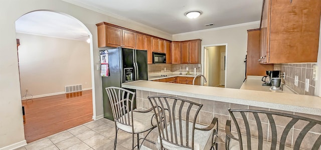 kitchen featuring light tile patterned floors, visible vents, arched walkways, crown molding, and black appliances