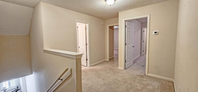 hallway with light carpet, baseboards, a textured ceiling, and an upstairs landing