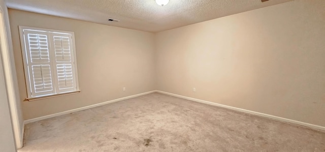 empty room with carpet, baseboards, and a textured ceiling